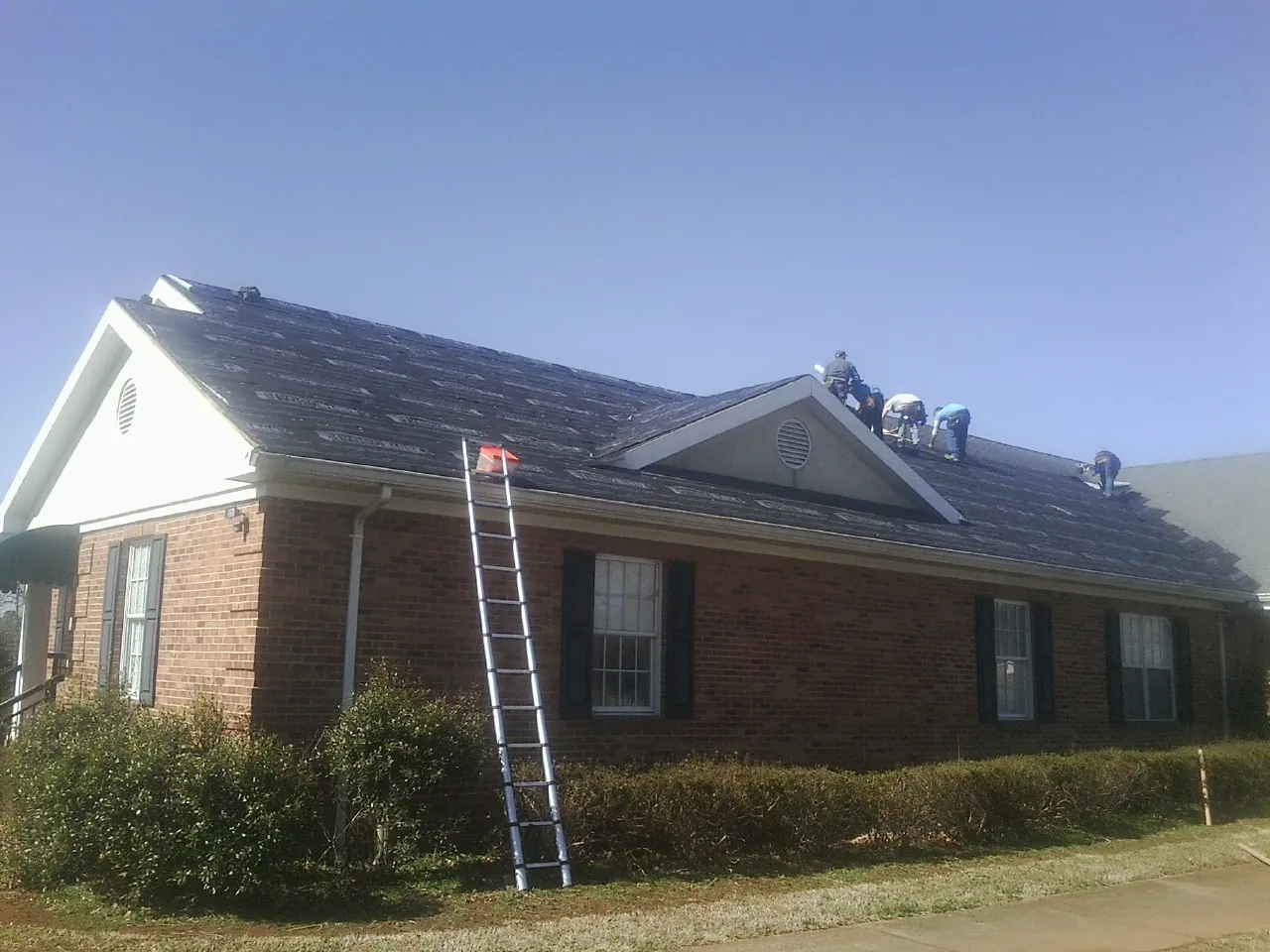 Crew tearing shingles off a brick ranch roof with a ladder set — Emergency Roof Repair work by our crew in Old Lyme