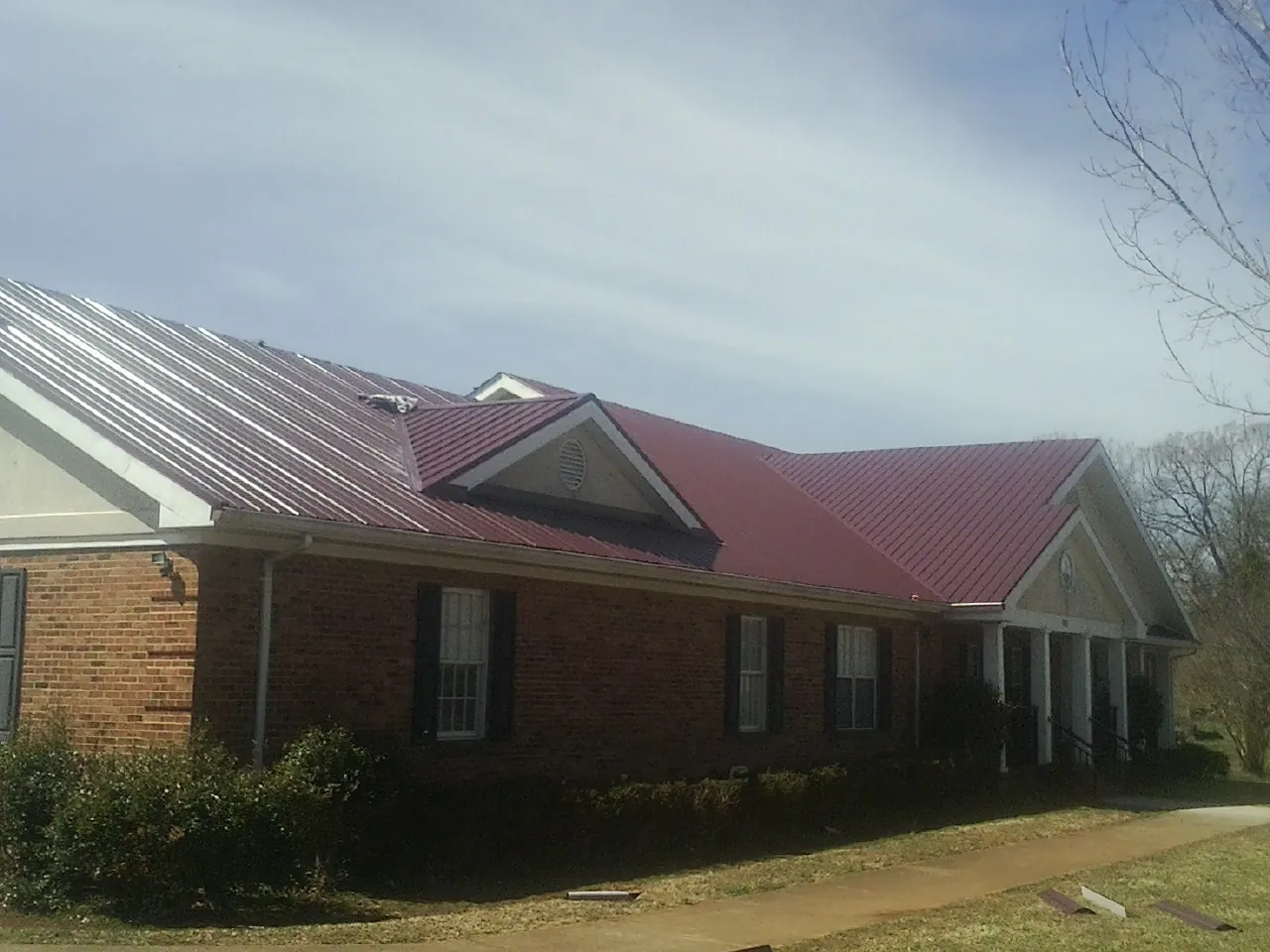 Red metal roof with gabled entries on a long brick building, from a Hail Damage Roof Repair job in Old Lyme