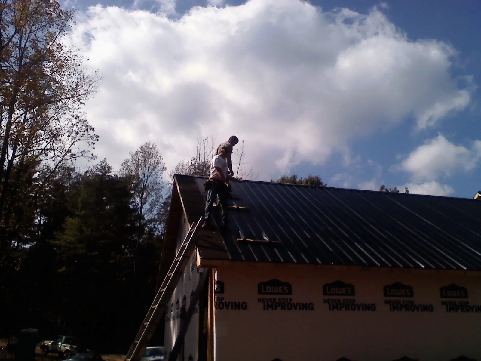 Roofer fastening dark metal panels high against a cloudy sky, from a Roof Inspection job in Old Lyme