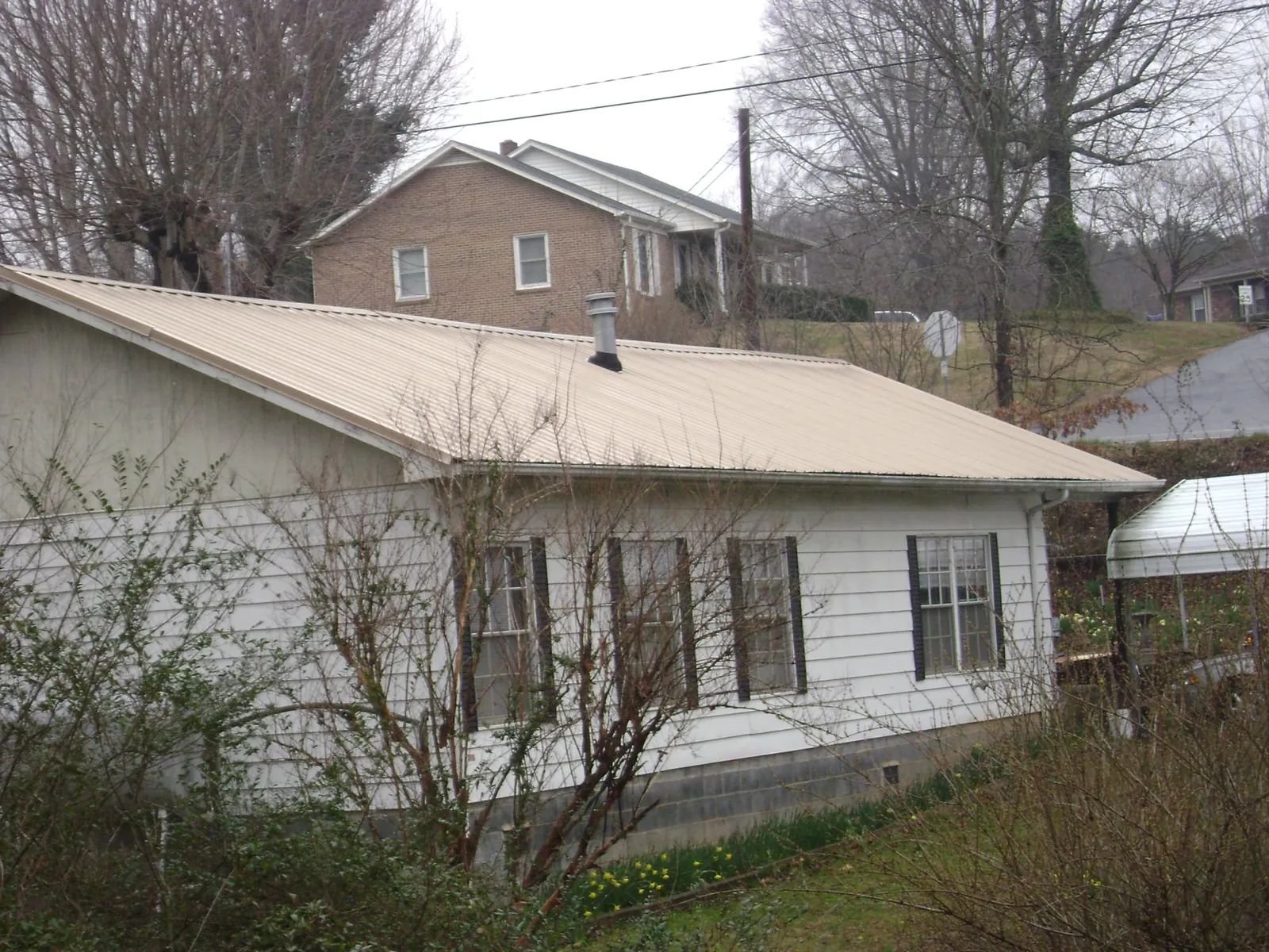 Tan metal roof on a white sided house set into a hillside — Commercial Roofing by Roofing Brothers in Old Lyme